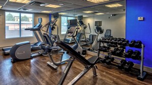 Une salle de sport équipée de divers appareils d’exercice, notamment des tapis de course, des vélos elliptiques et un porte-haltères.