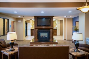 A hotel lobby with a fireplace, seating area, and a television mounted above it.