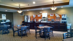 A breakfast area with tables and chairs, a counter with food and drink dispensers, and a sign indicating breakfast options.