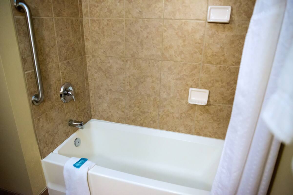 A bathroom with a bathtub, a handrail, and a white towel.