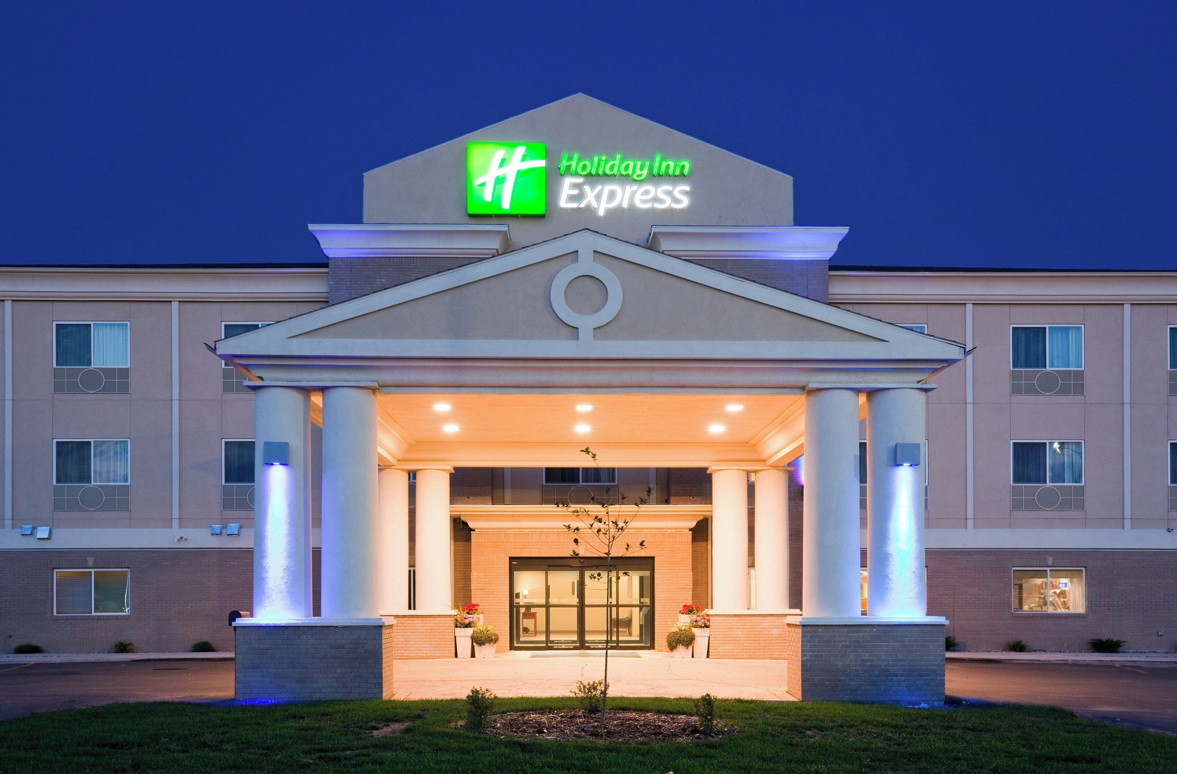 Edificio de Holiday Inn Express con entrada central, amplias columnas y un logotipo verde destacado.