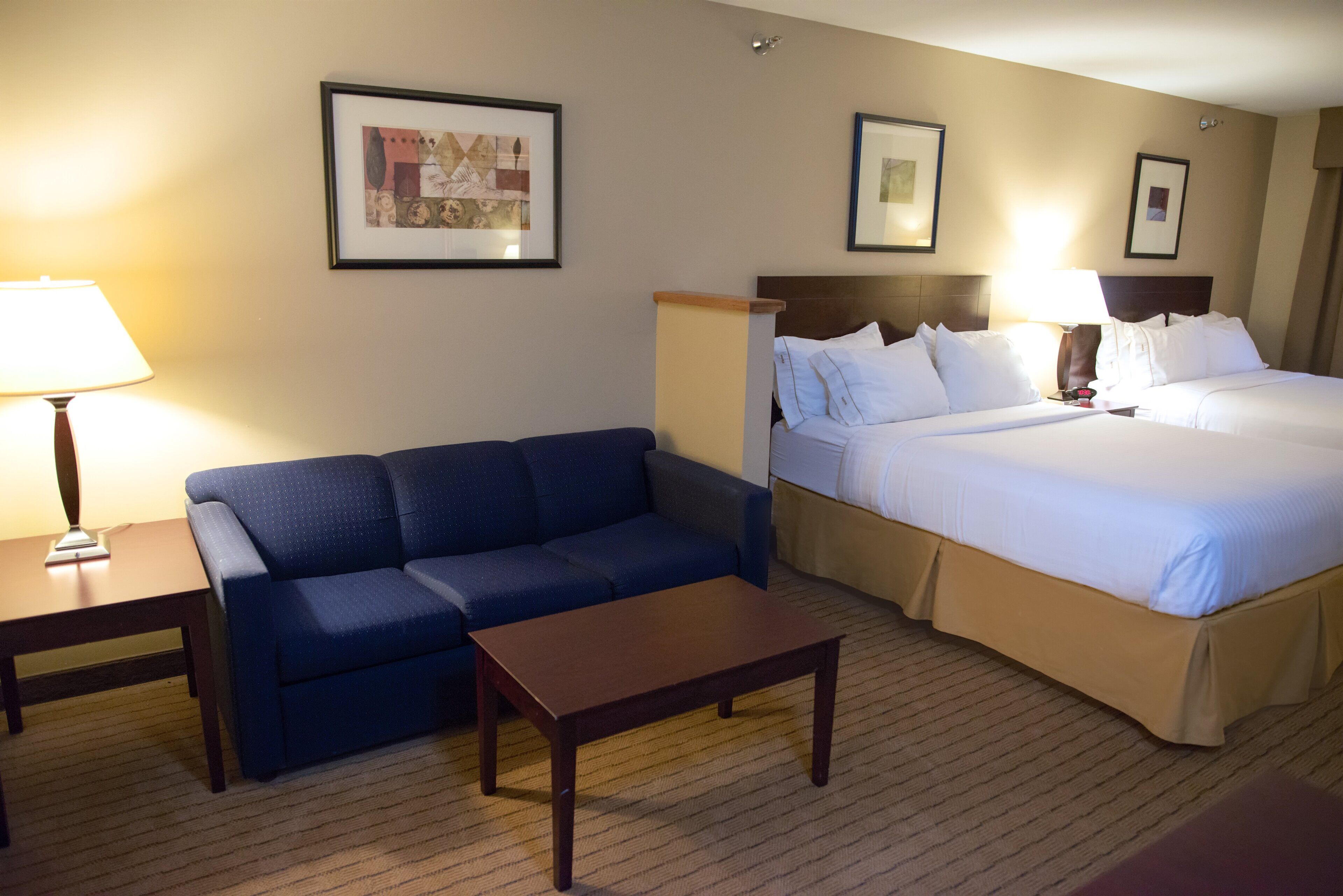 Quarto de hotel com cama, sofá, mesa pequena e duas luminárias.