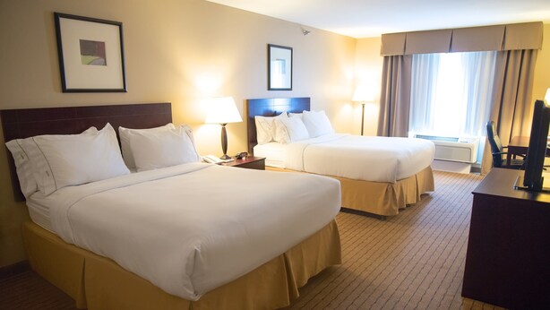 A hotel room with two queen beds, a desk, a chair, and a television.