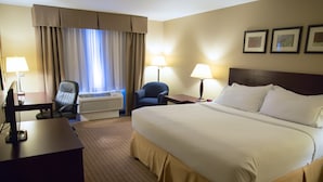A hotel room with a large bed, two chairs, a desk, a lamp, and a window with curtains.