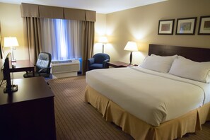 A hotel room with a large bed, two chairs, a desk, a lamp, and a window with curtains.
