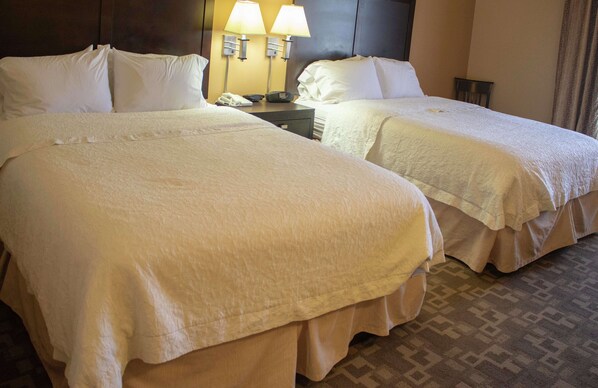 Habitación de hotel con dos camas, una mesita de noche con teléfono y lámpara, y una alfombra estampada.