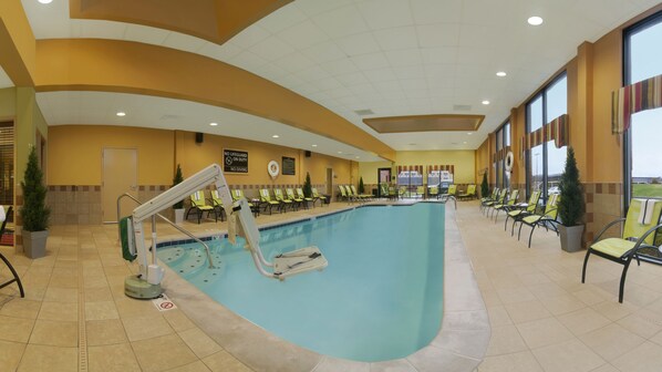 Una piscina interior con una silla de salvavidas, sillas junto a la piscina y un cartel de prohibido bucear.