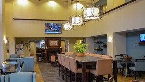 Een hotel lobby met een eetgedeelte, een aan de muur bevestigde televisie en een bloempot op de tafel.