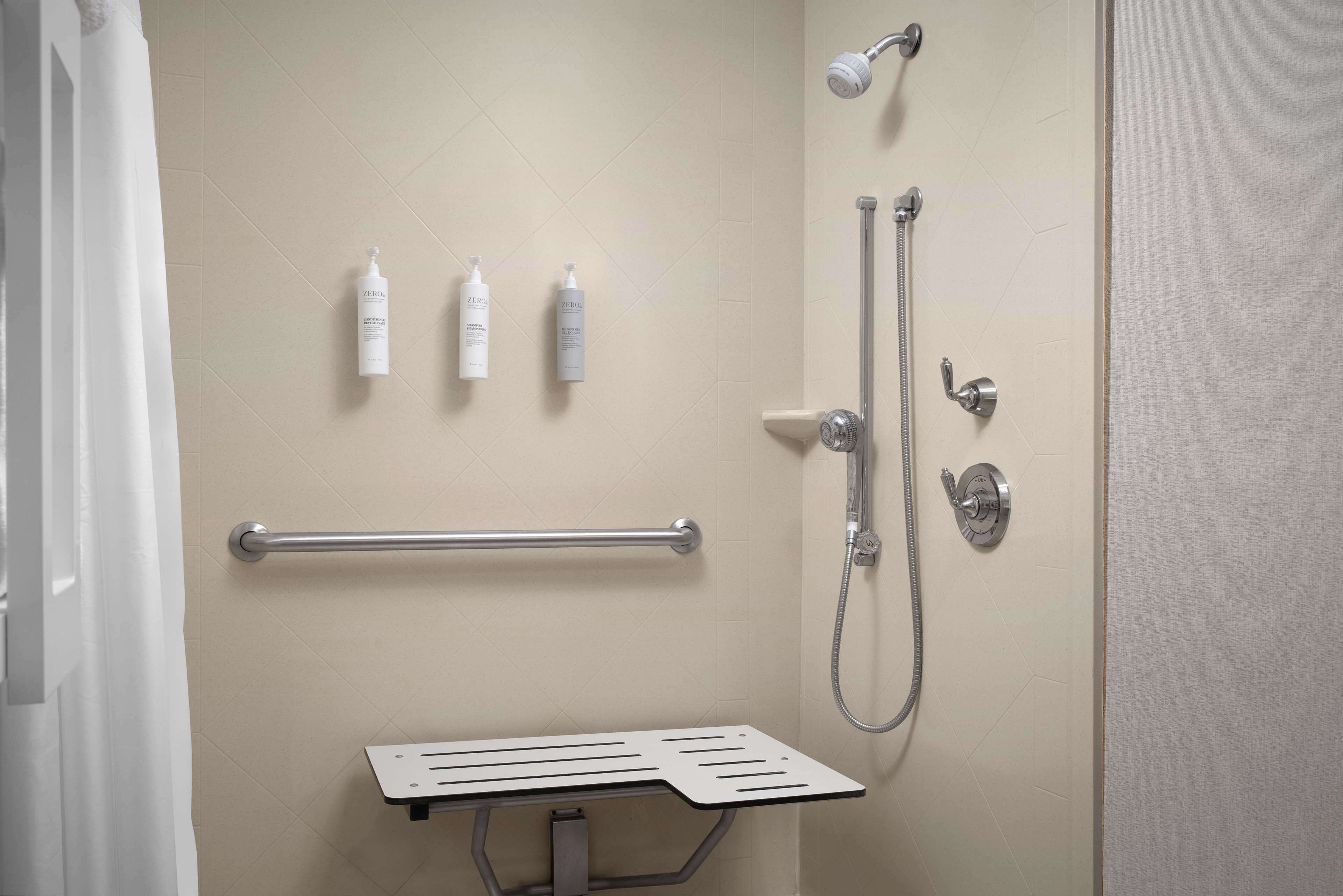 A bathroom with a shower, grab bars, and toiletries on the wall.