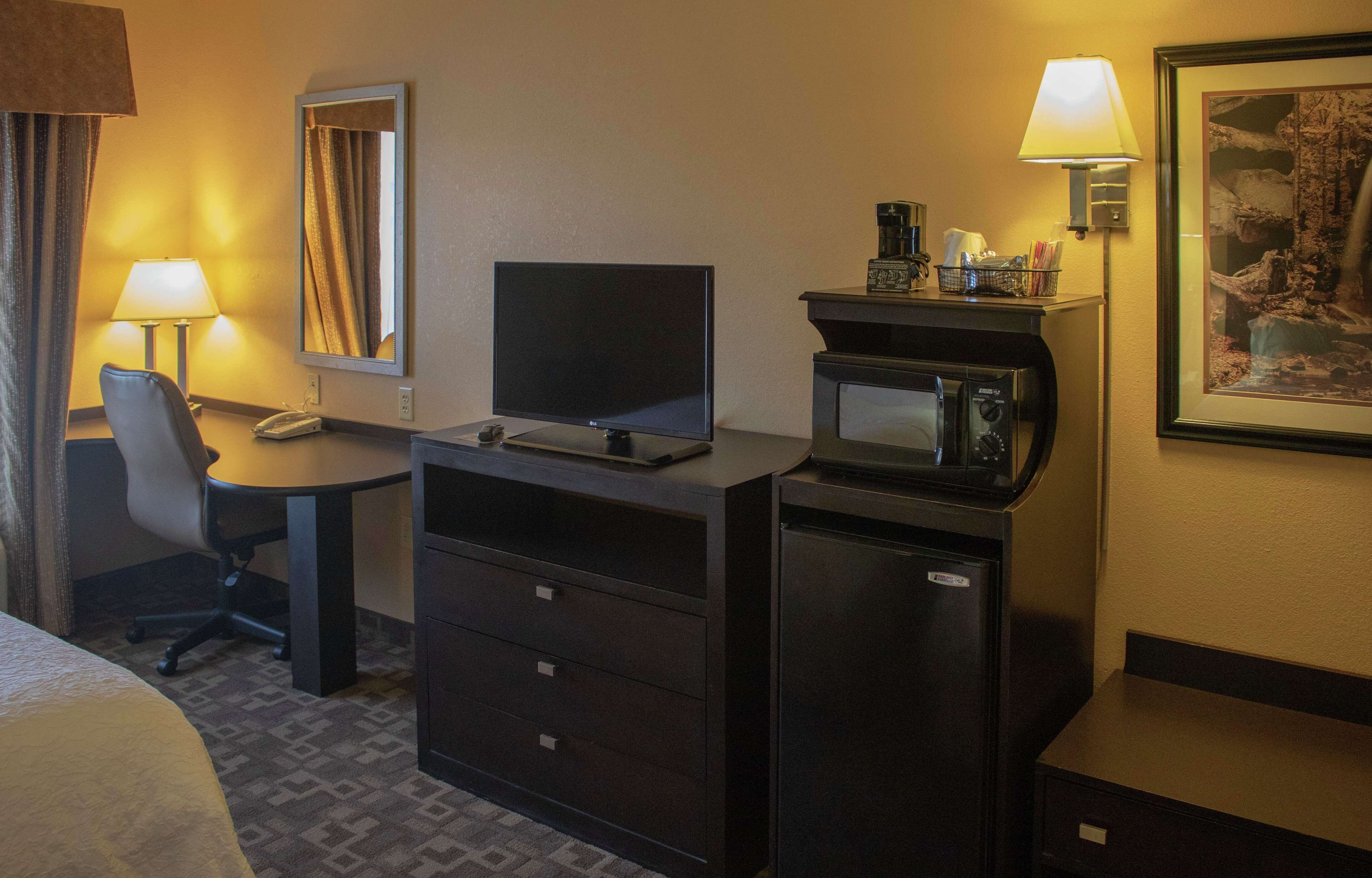 A hotel room with a bed, a desk with a computer and a telephone, a chair, a microwave, and a coffee maker.
