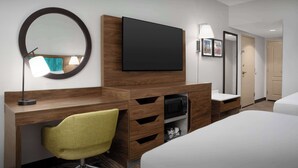 Hotelkamer met een bed, een bureau met stoel, een televisie, een spiegel, een magnetron en een deur.