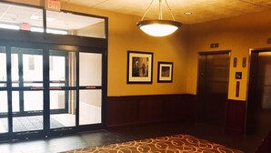 An interior hallway with a patterned carpet, an exit door, framed pictures on the wall, and an elevator. - Hampton Inn & Suites Chesapeake-Battlefield Blvd. (Chesapeake)