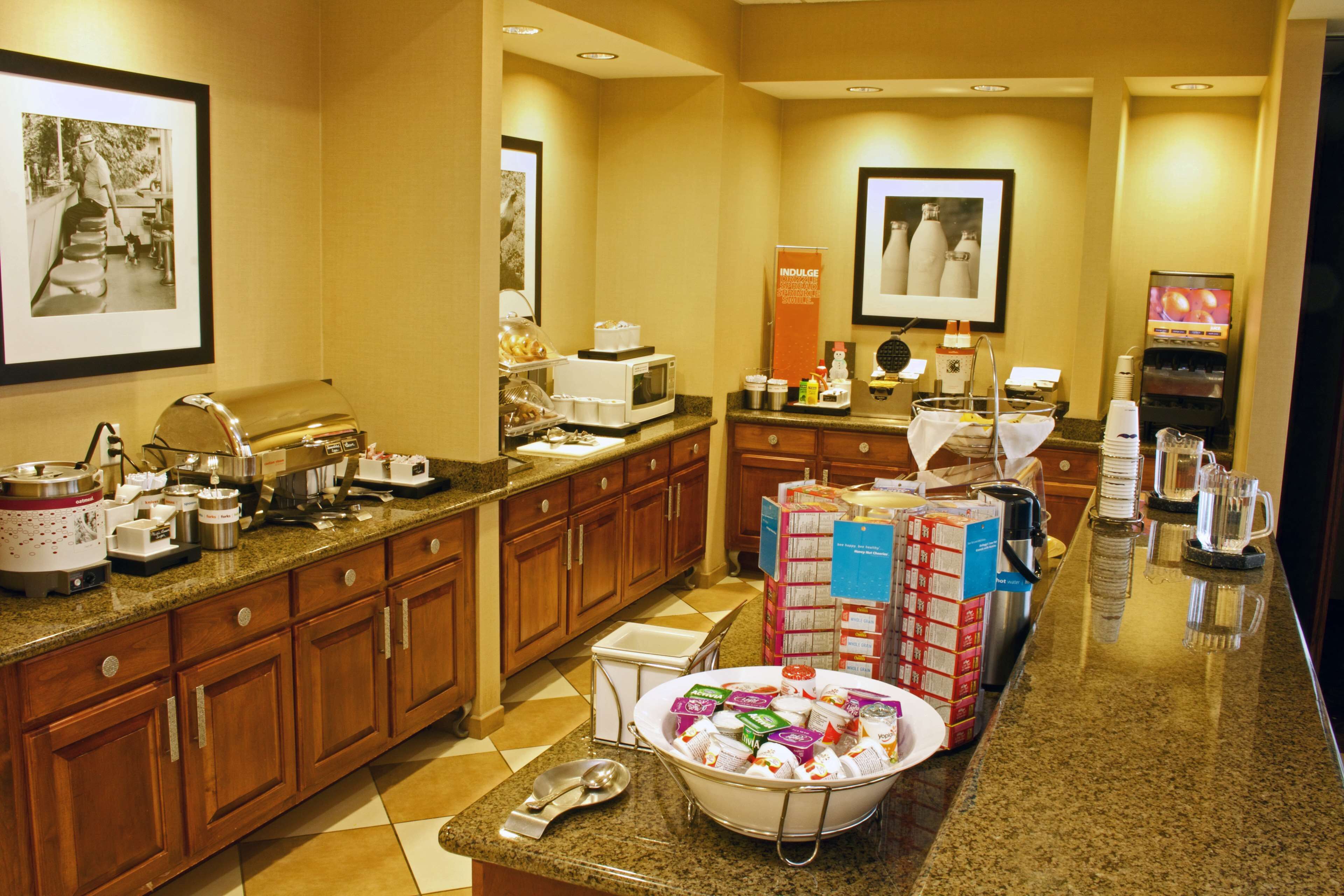 A hotel kitchen with wooden cabinets, a granite countertop, a microwave, a coffee maker, and a bowl of packaged food items.