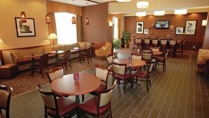 A hotel lobby with multiple seating areas, including sofas, chairs, and round tables. There are wall-mounted lamps, a television, and framed pictures on the walls. - Hampton Inn & Suites Chesapeake-Battlefield Blvd. (Chesapeake)