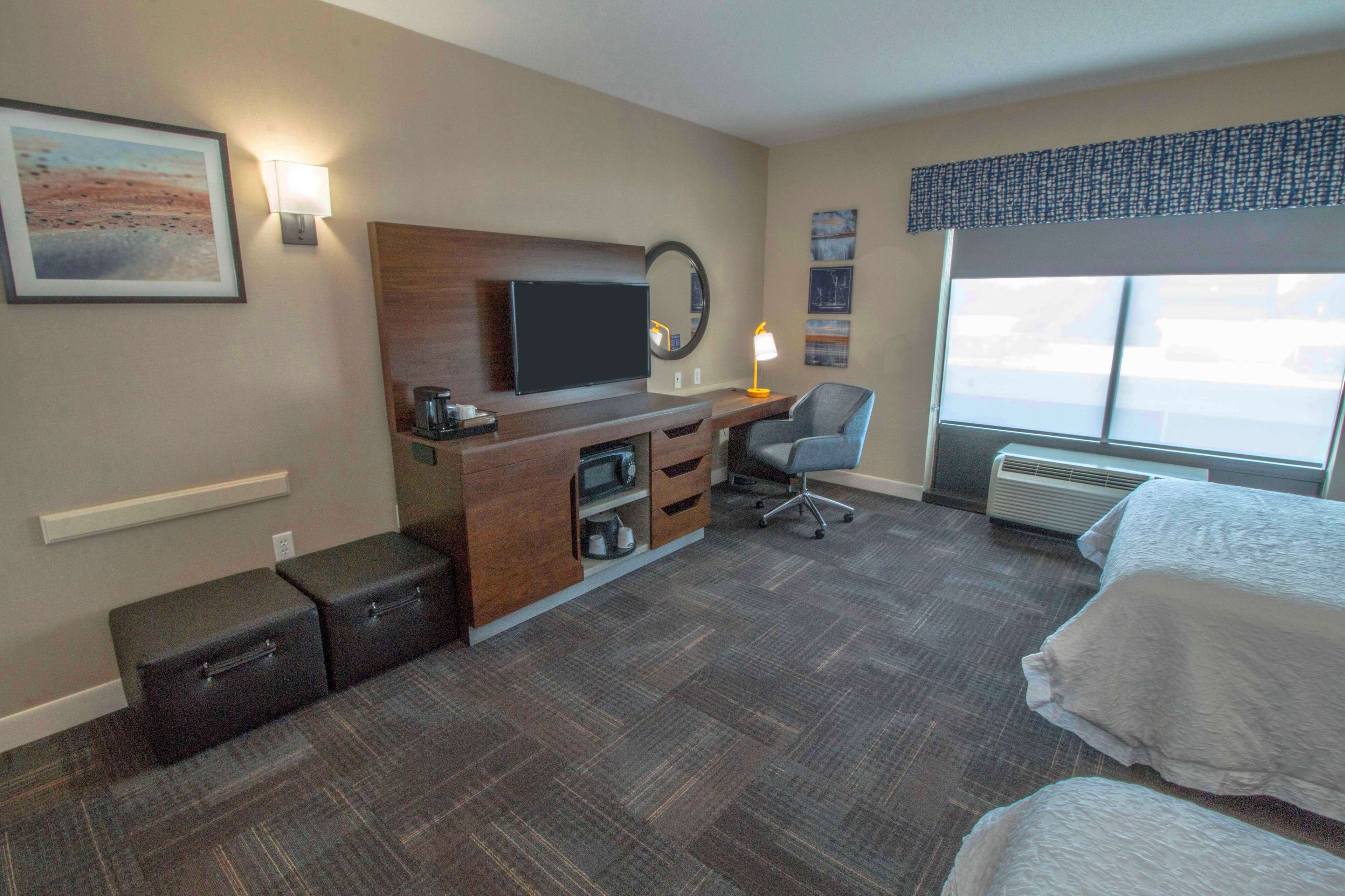 Une chambre d’hôtel comprenant un lit, un bureau avec un ordinateur, une chaise, une télévision, un radiateur et une fenêtre.