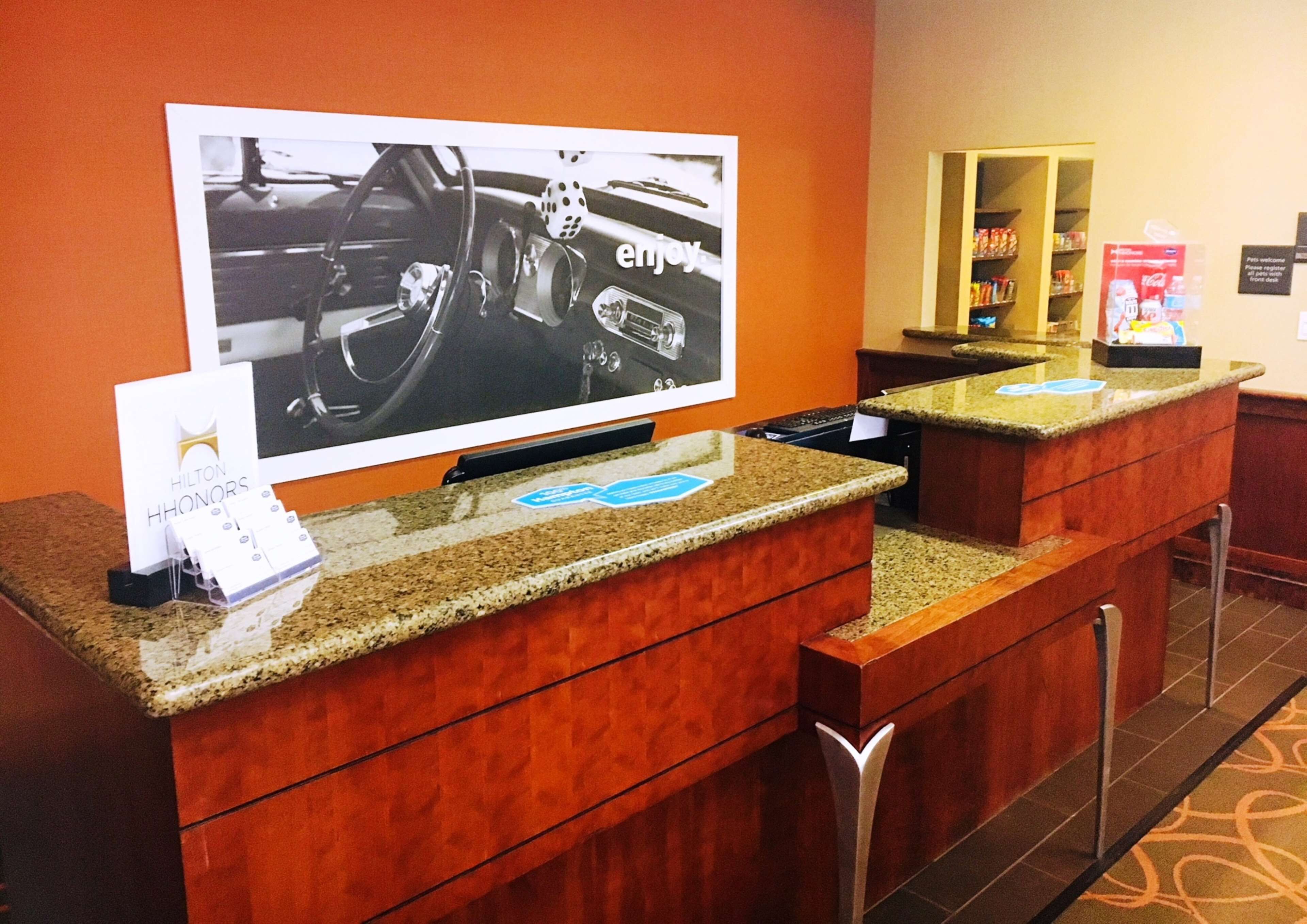 A hotel reception area with a large screen displaying a car interior, a counter with a card holder, and a minibar.