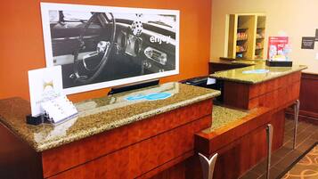 A hotel reception area with a large screen displaying a car interior, a counter with a card holder, and a minibar.