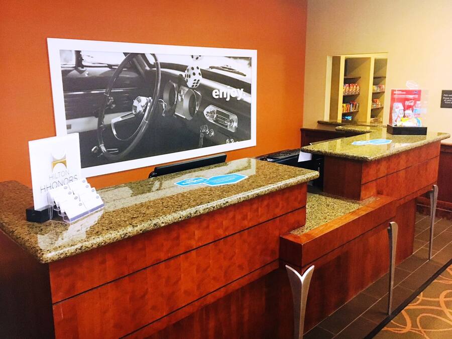 A hotel reception area with a large screen displaying a car interior, a counter with a card holder, and a minibar.