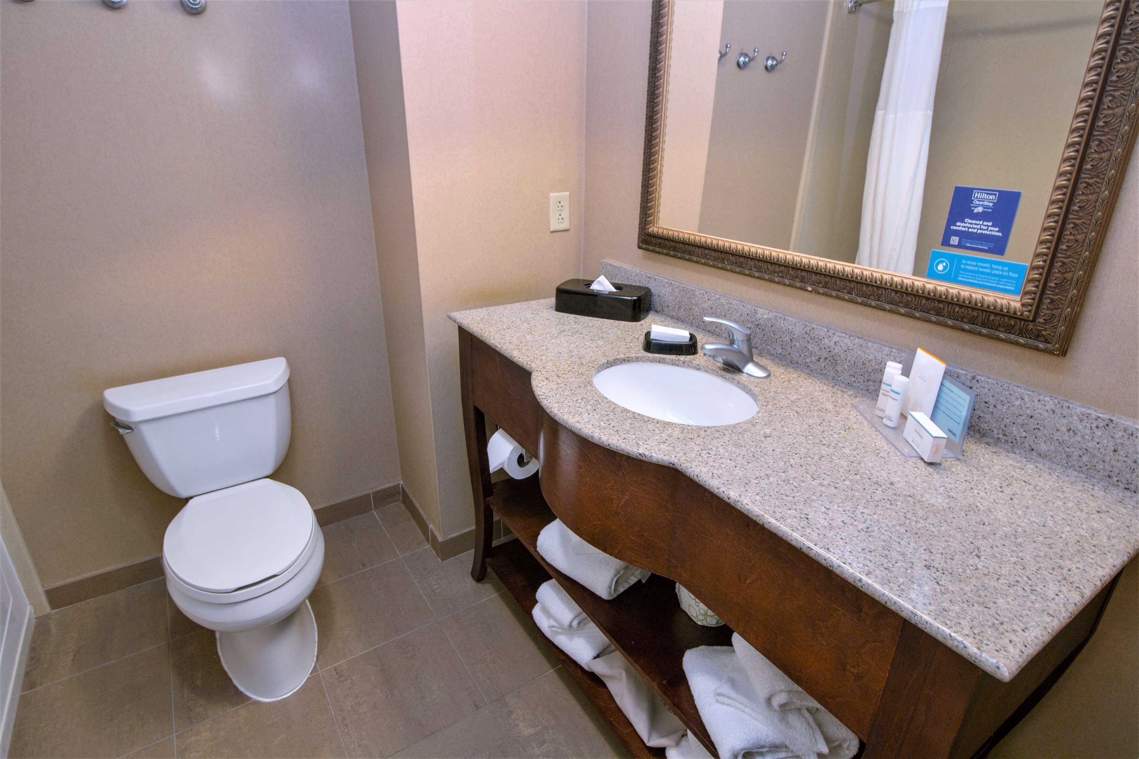 Un baño con inodoro blanco, lavabo con encimera de granito y espejo con marco decorativo.