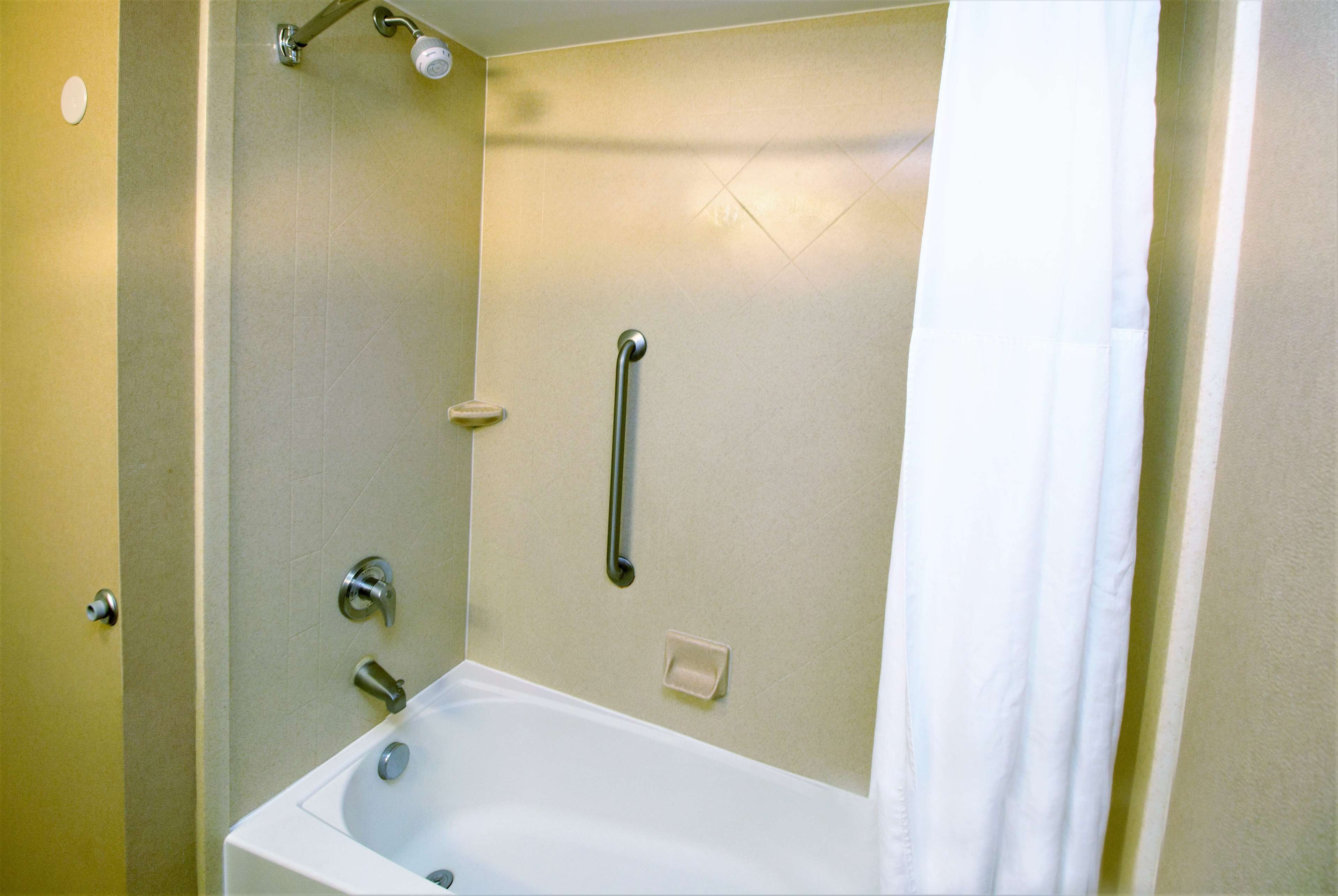 A bathroom with a bathtub, a shower, and a handrail.