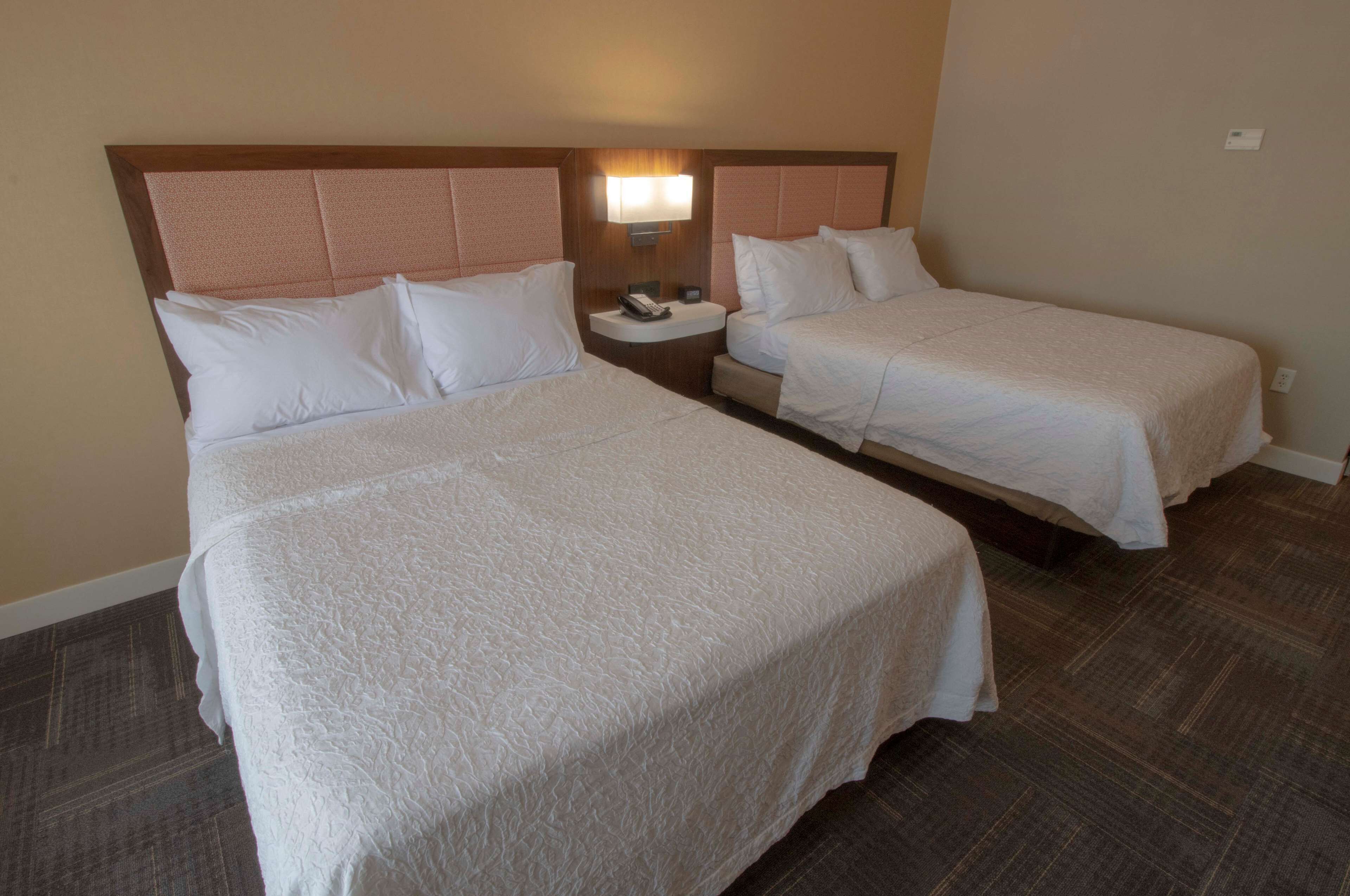 A hotel room with two beds, a nightstand with a lamp, and a telephone.