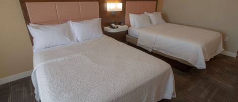 A hotel room with two beds, a nightstand with a lamp, and a telephone.
