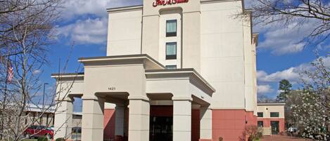 A Hampton Inn & Suites building with a beige facade, a red entrance, and a clear blue sky.