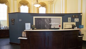A reception desk with a 'Explore' sign, a telephone, and a 'Manager On Duty' sign.