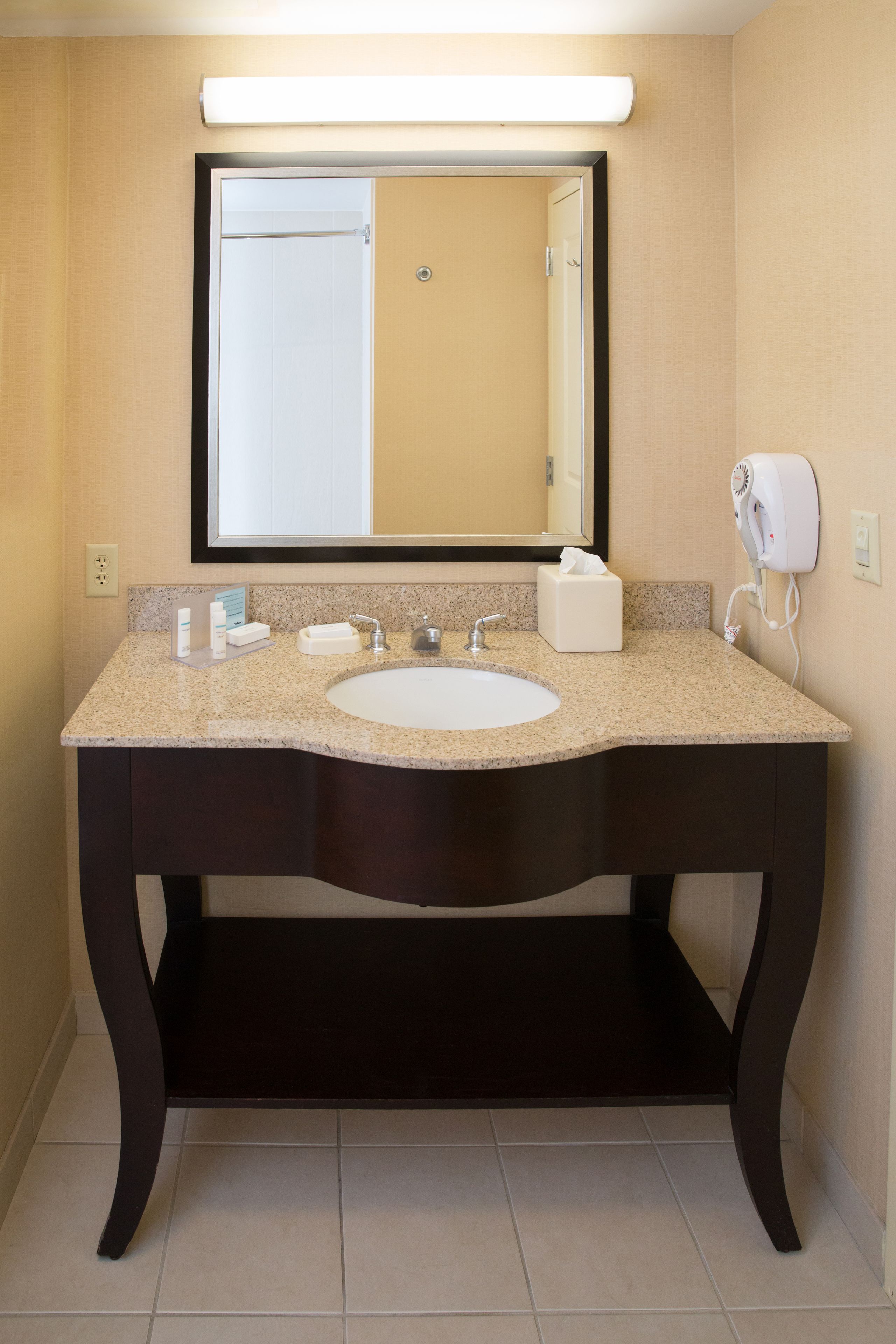 A bathroom with a granite countertop sink, a mirror, a towel dispenser, and a soap dispenser.