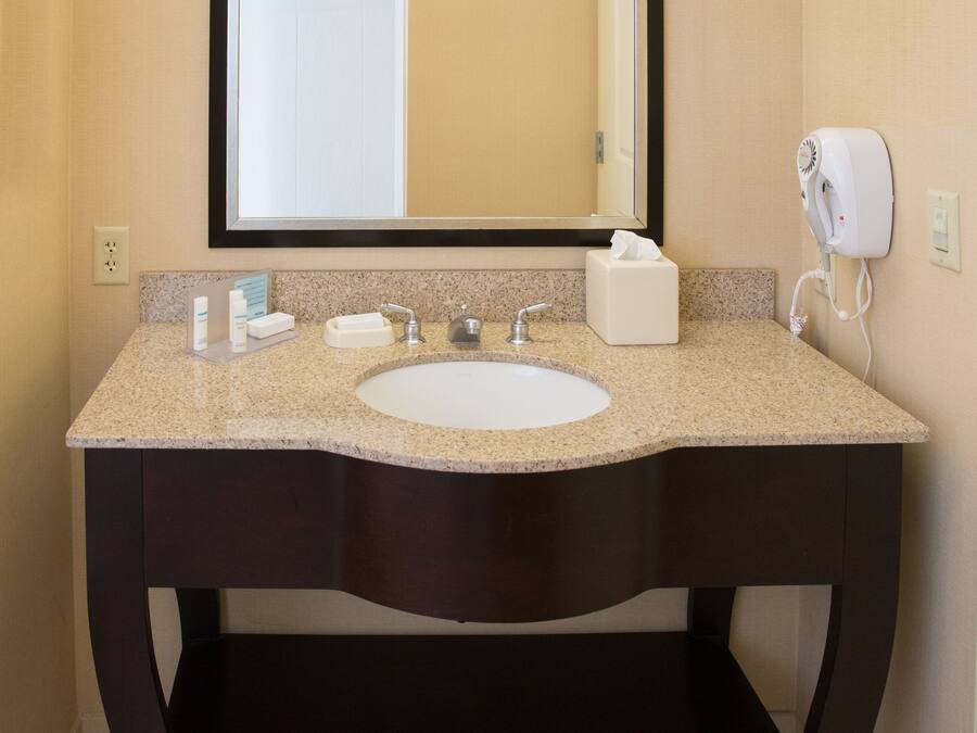 A bathroom with a granite countertop sink, a mirror, a towel dispenser, and a soap dispenser.