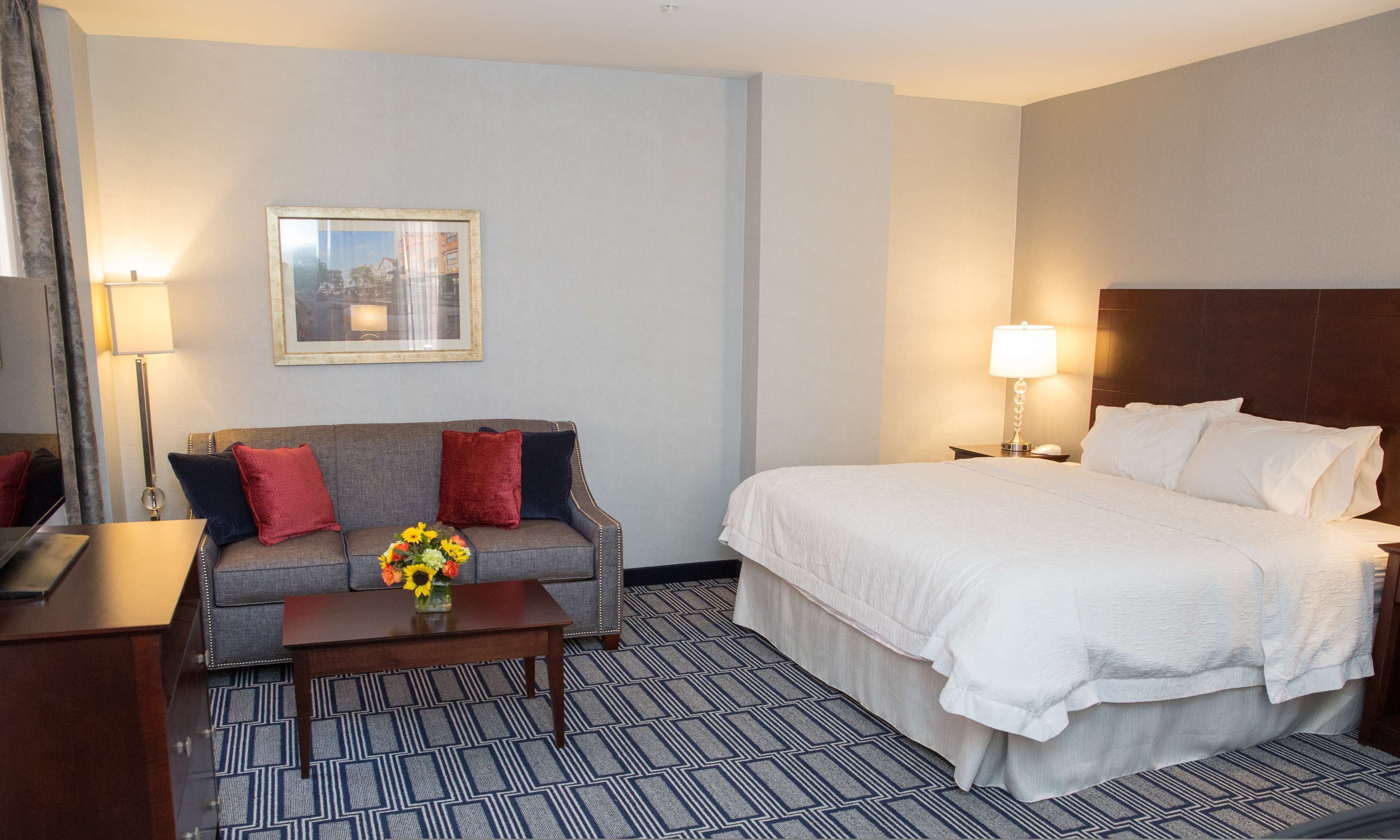 A hotel room with a bed, a sofa, a coffee table with flowers, a lamp, and a framed picture on the wall.