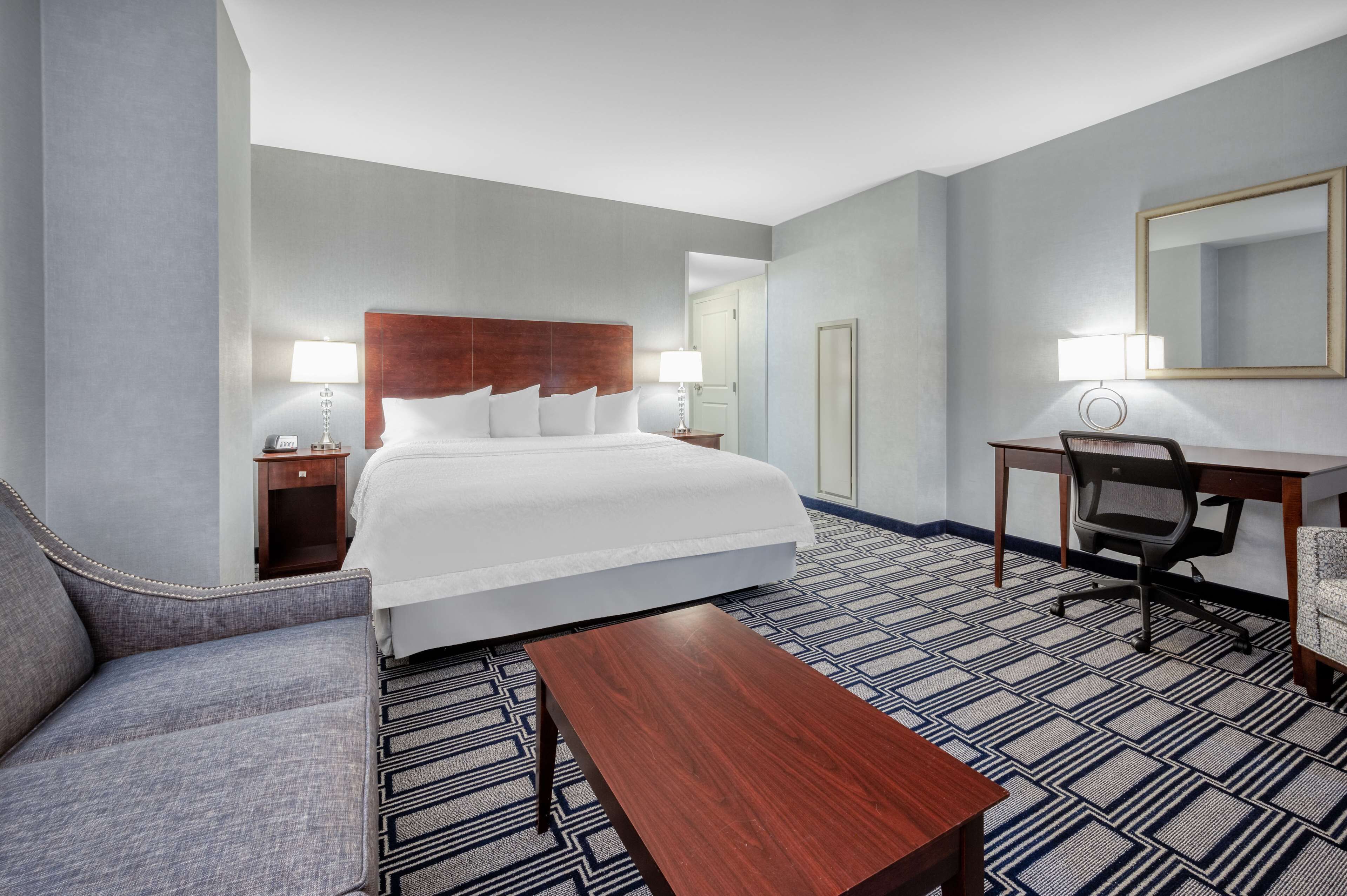 A hotel room with a bed, a desk, a chair, a sofa, and a coffee table.