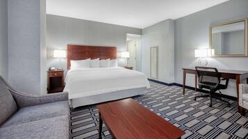 A hotel room with a bed, a desk, a chair, a sofa, and a coffee table.