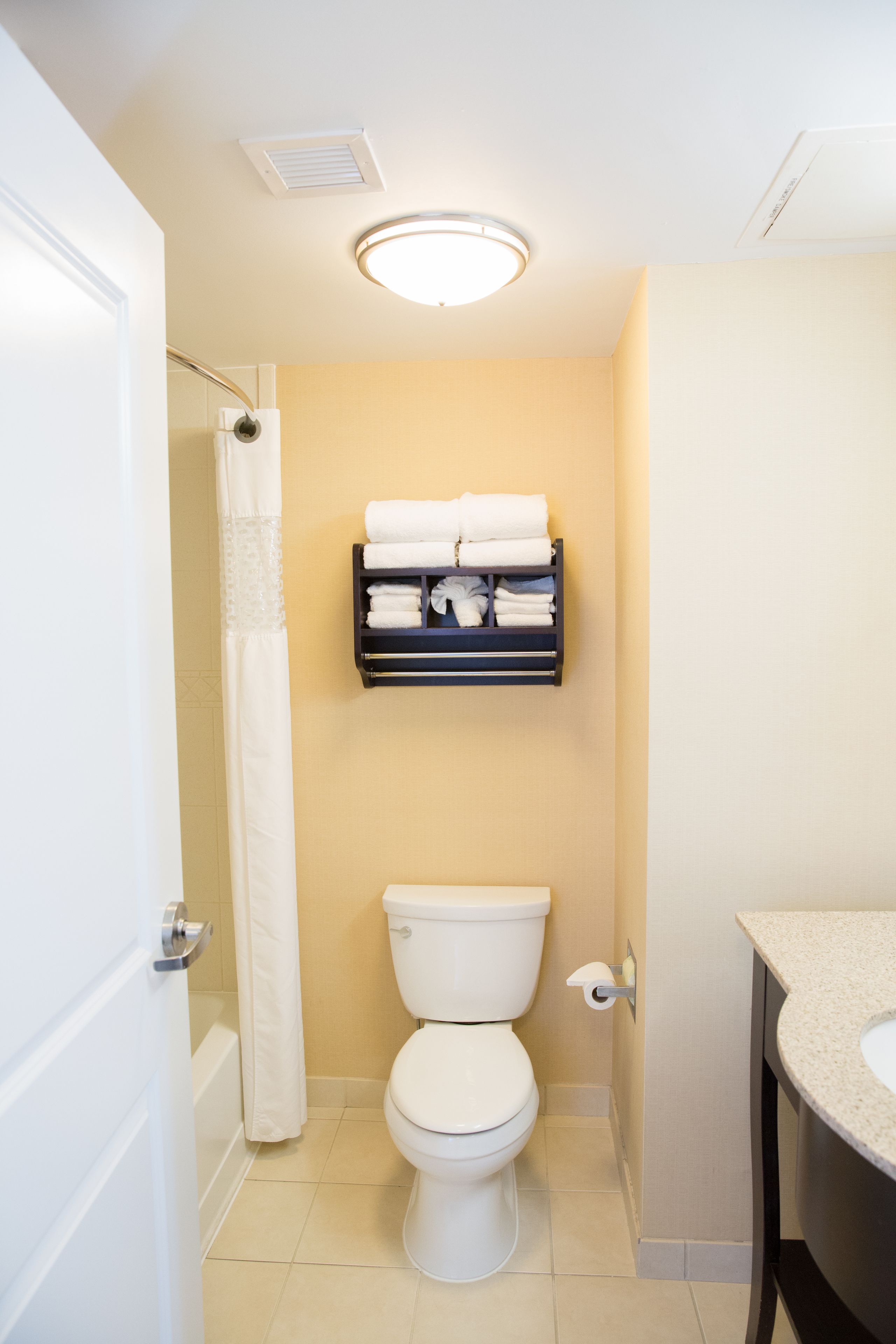 A bathroom with a toilet, a shower curtain, a towel rack with towels, and a sink.