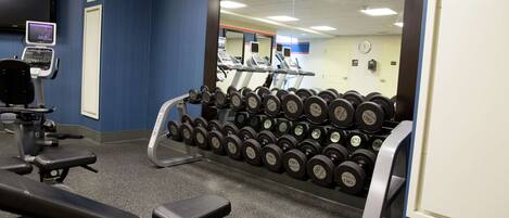 A gym with exercise equipment, a wall-mounted TV, and a mirror reflecting treadmills.