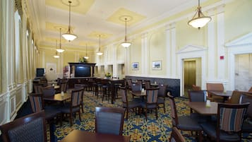 Un hall de hotel con varias mesas y sillas para comer, una recepción y un televisor.