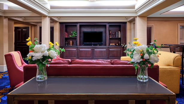 A spacious living room with a red sofa, two vases of flowers, a flat-screen TV, and a bookshelf.