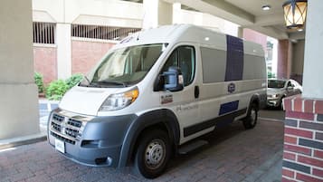 A white van parked in a covered parking area with a brick wall and a metal railing in the background.