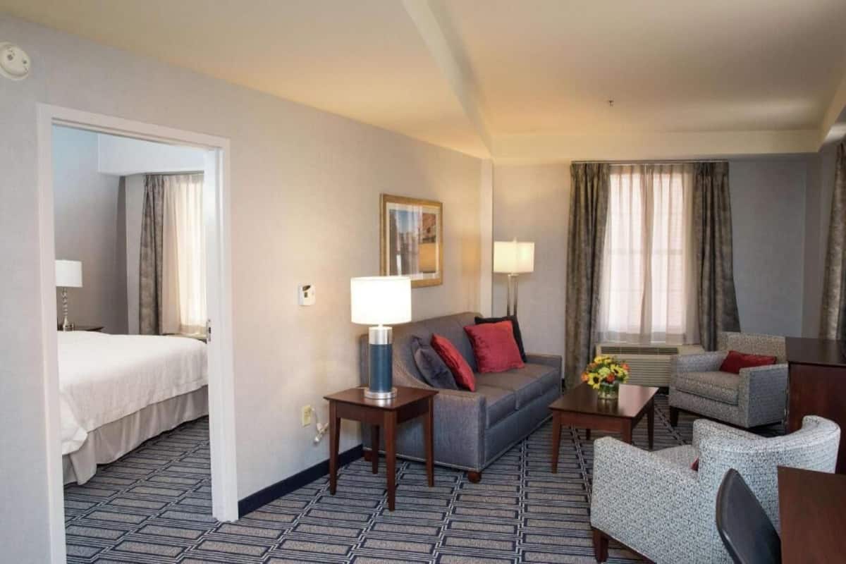Une chambre d’hôtel avec un lit, un canapé, une chaise, une table basse et une lampe.