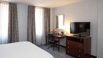 A hotel room with a large bed, a desk with a chair, a television, and a mirror.