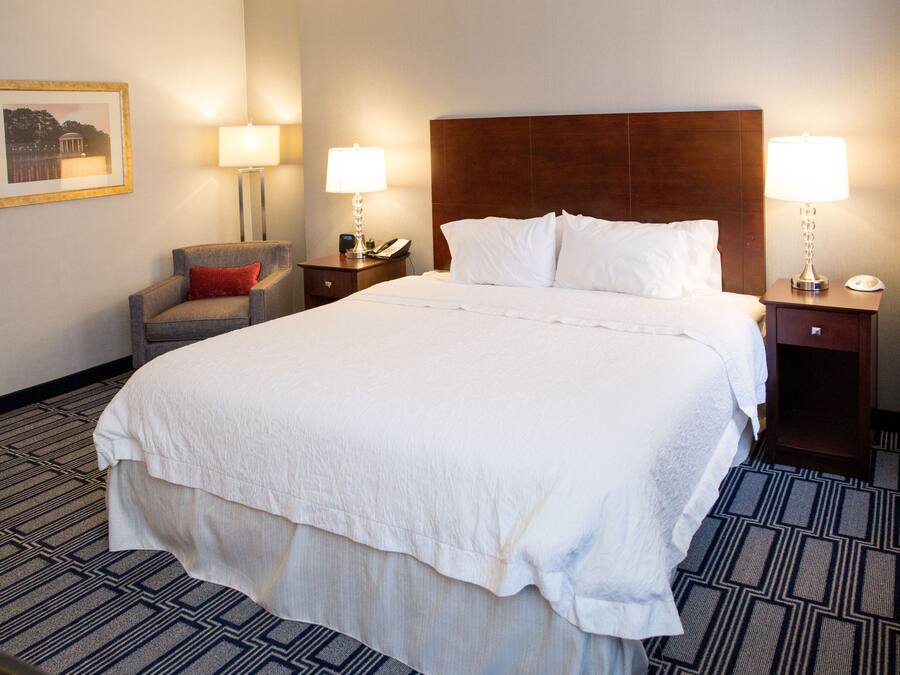 A hotel room with a large bed, two bedside tables with lamps, a chair, and a framed picture on the wall.