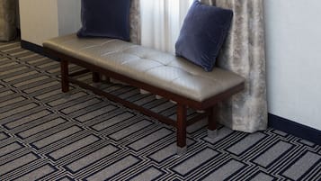 A room with a bench, two pillows, a patterned carpet, and a painting on the wall.
