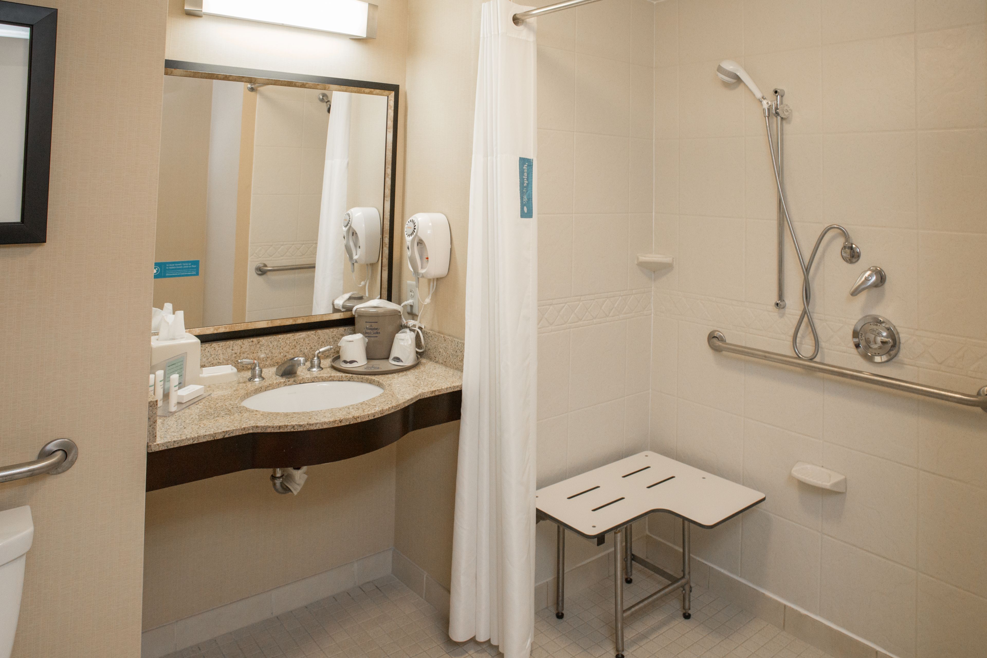 A bathroom with a sink, mirror, shower, and a small stool.