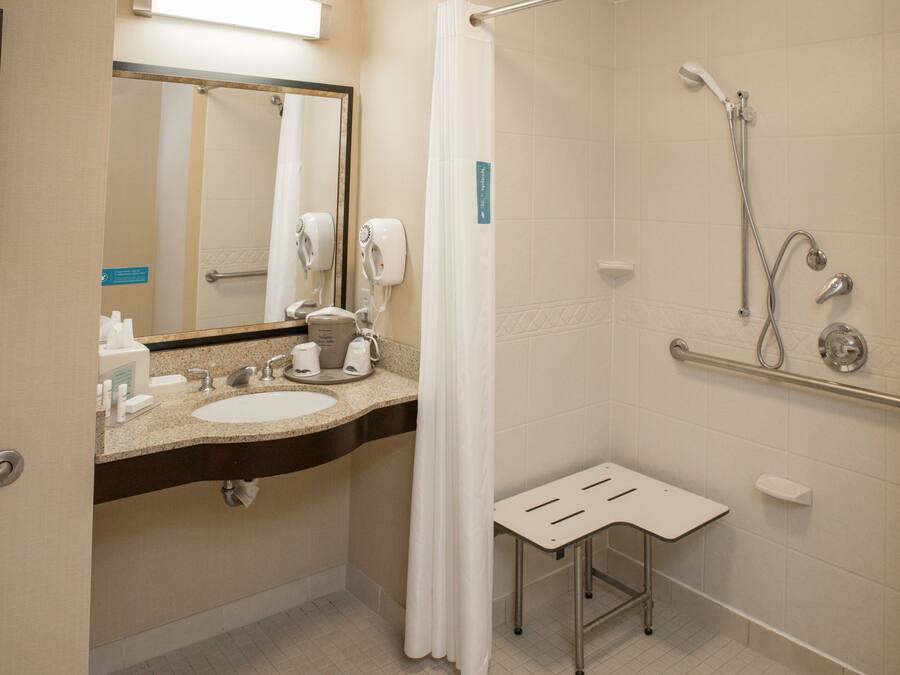 A bathroom with a sink, mirror, shower, and a small stool.