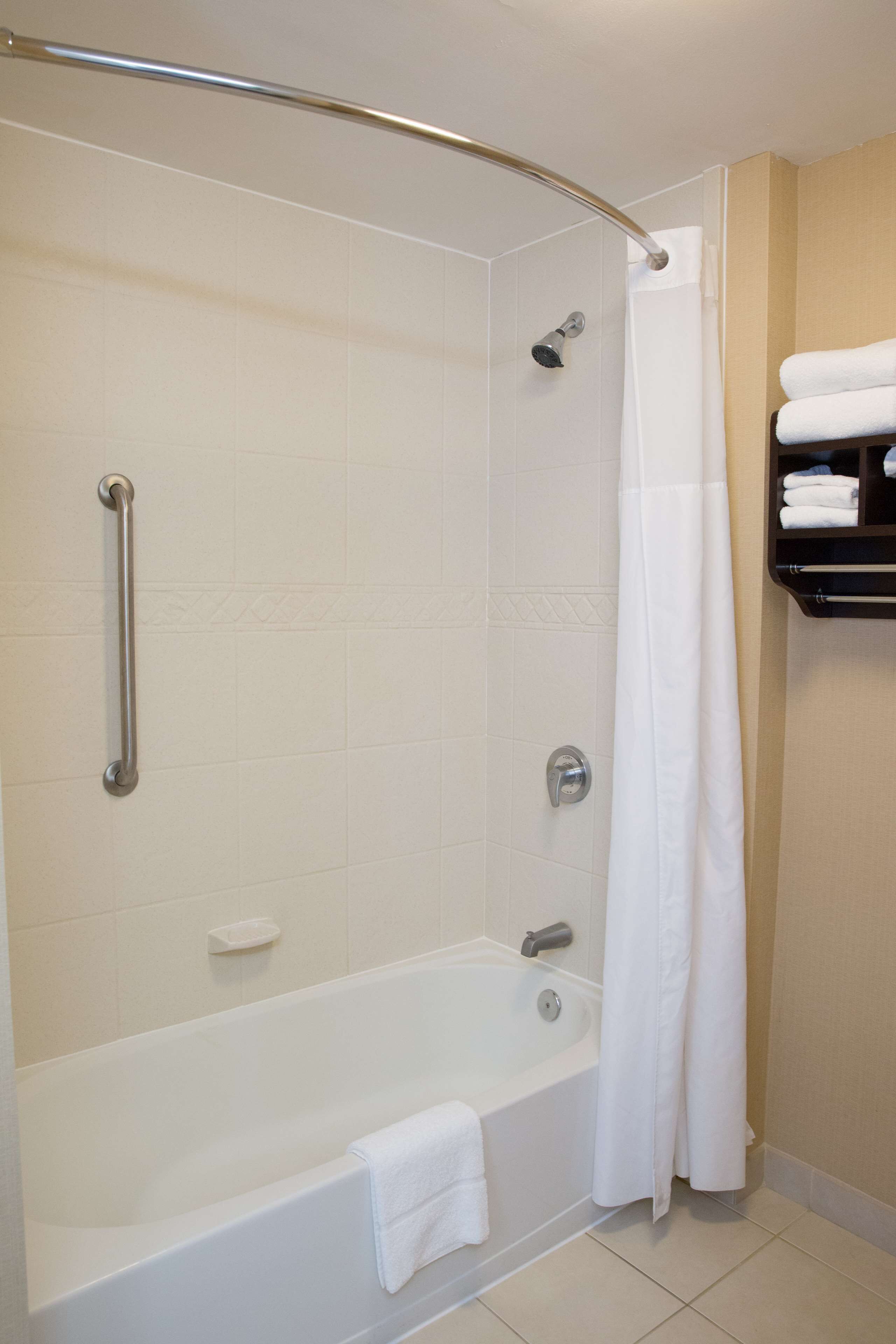 Un baño moderno con cabina de ducha, barra de apoyo y repisa con toallas.