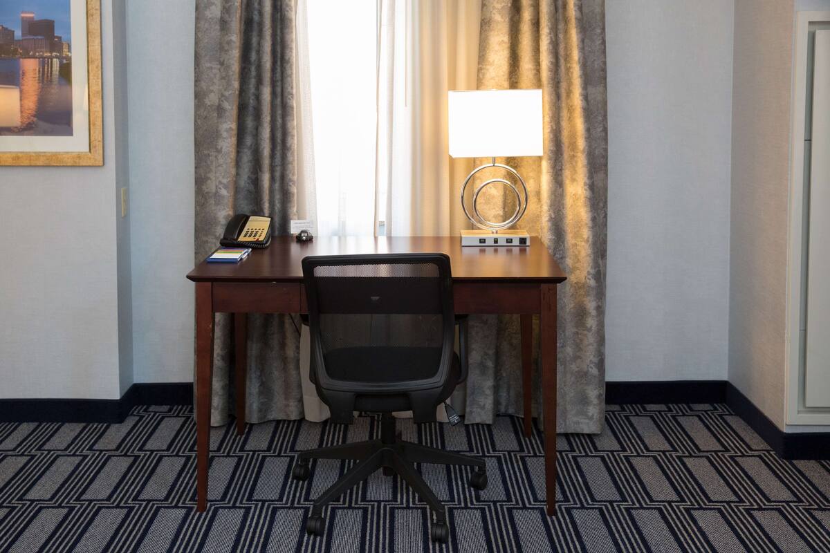 Une chambre d’hôtel équipée d’un bureau, d’une chaise, d’une lampe et d’un tableau encadré au mur.