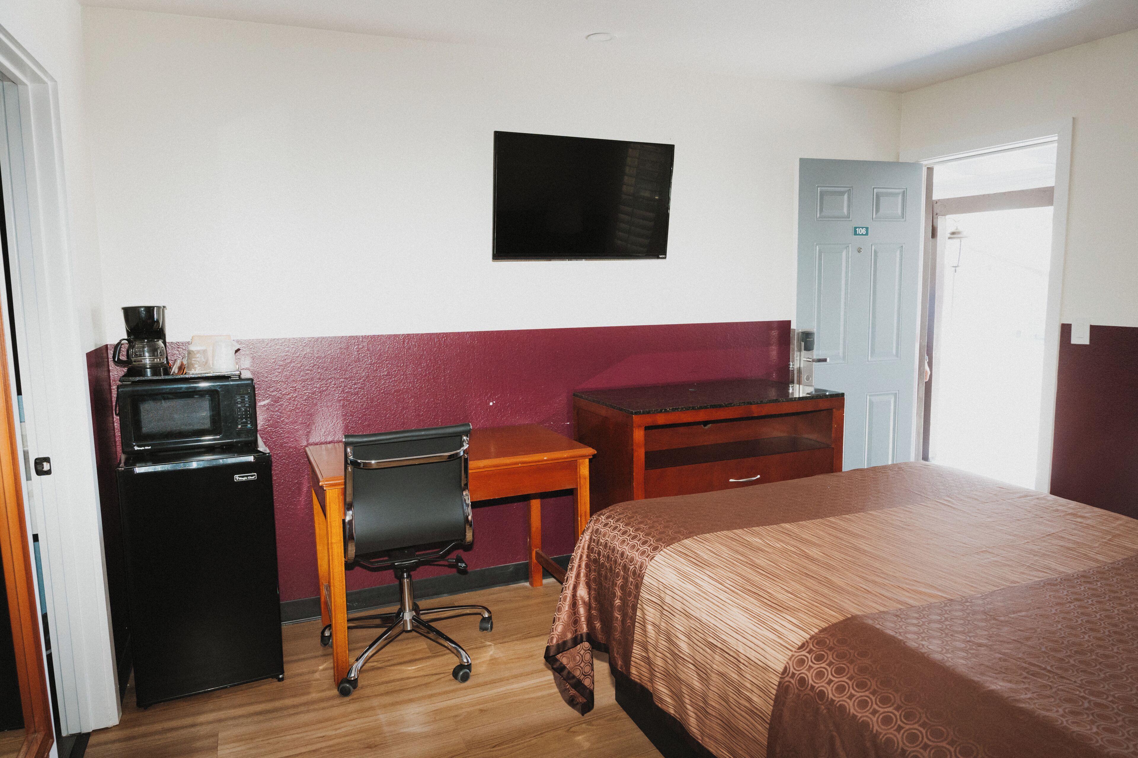 A hotel room with a bed, a desk, a chair, a microwave, and a television.
