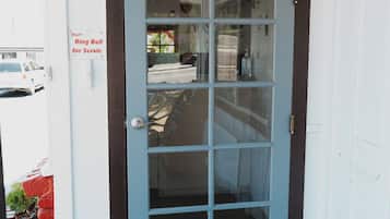 A front door with a 'hello' mat, a 'Ring Bell for Servic' sign, and a view of the street through the glass panels.