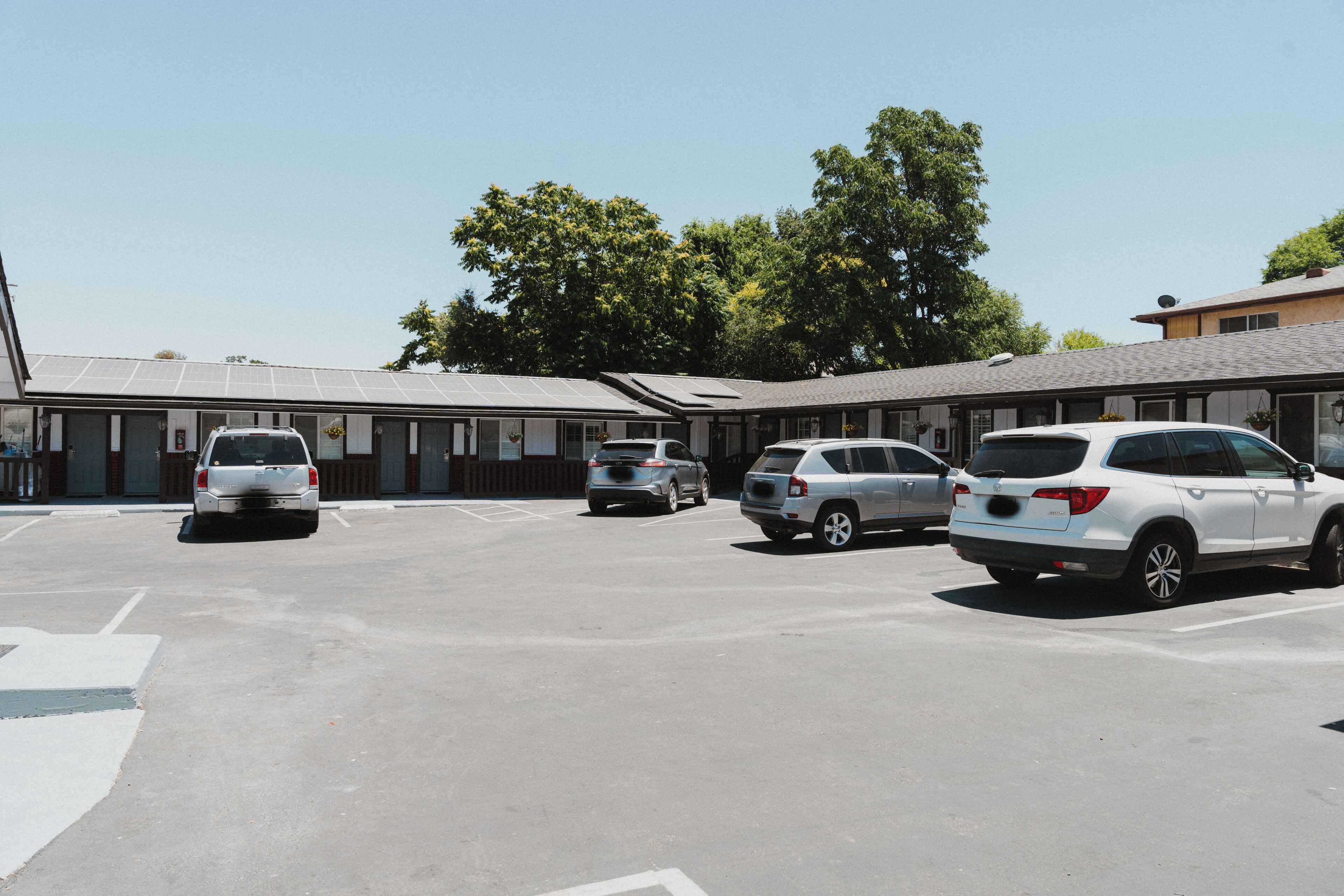 A parking lot with several cars, a building with a flat roof, and trees in the background.