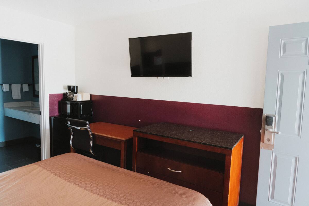 Habitación de hotel con cama, escritorio, televisor montado en la pared y una puerta.